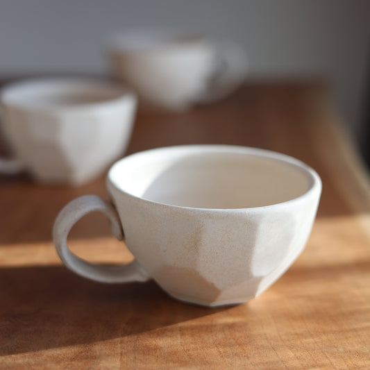 White faceted ceramic cup with textured surface on a wooden surface