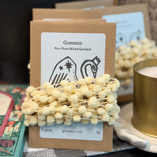 Gravesco pom pom wired garland on a brown card with a blurred background