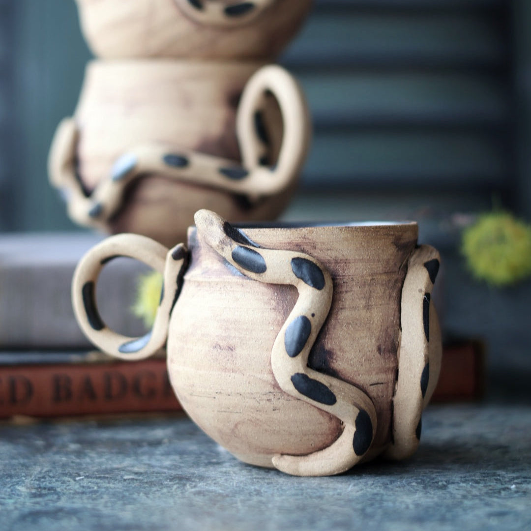 Stack of ceramic mugs with unique designs on a textured surface