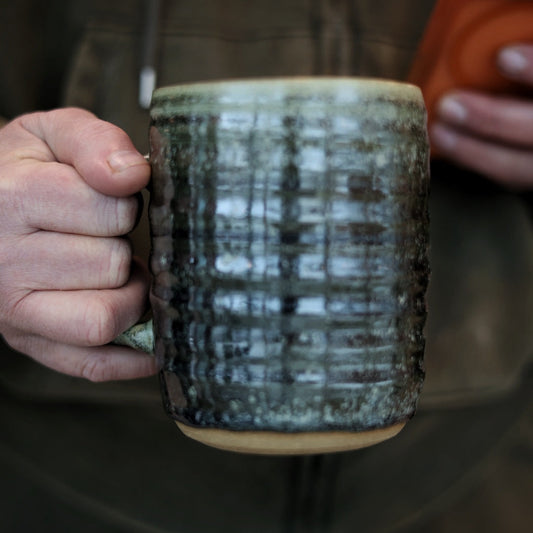 Person holding a textured ceramic mug with a blurred background