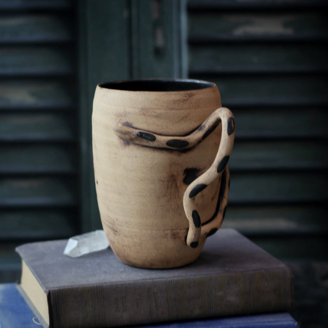 Ceramic mug with a unique handle on top of books against a dark background