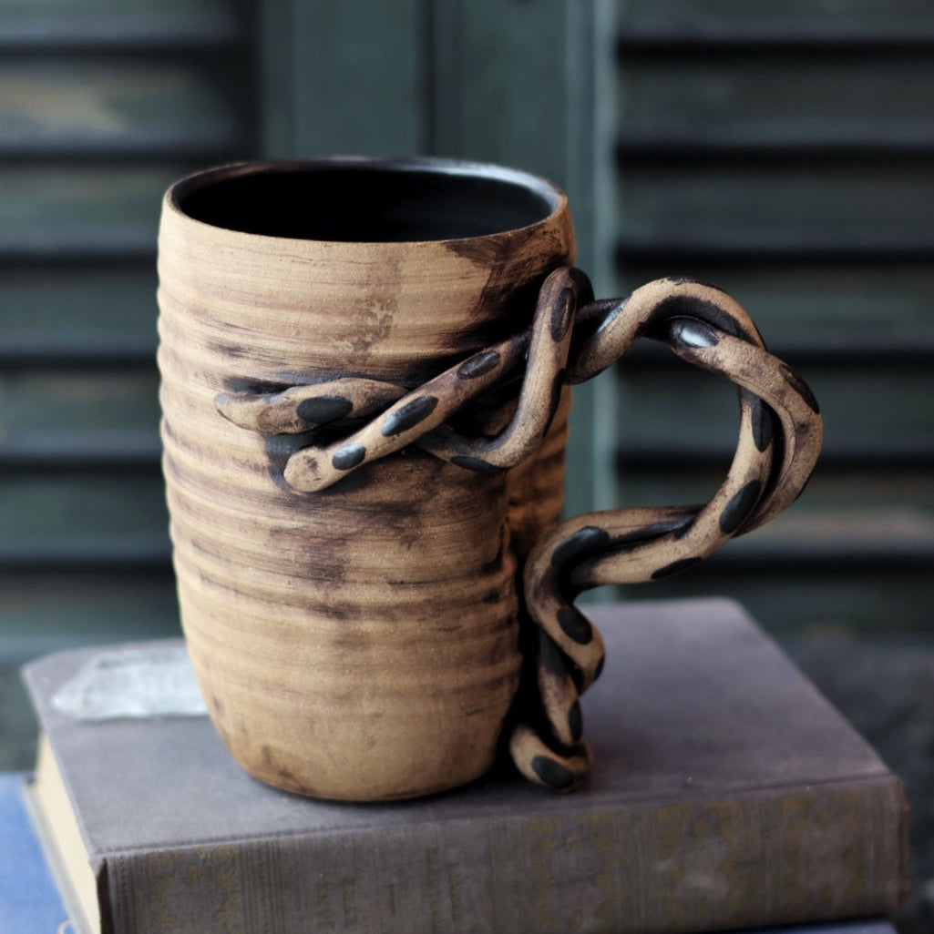 Ceramic mug with a unique handle design on top of books against a blurred background