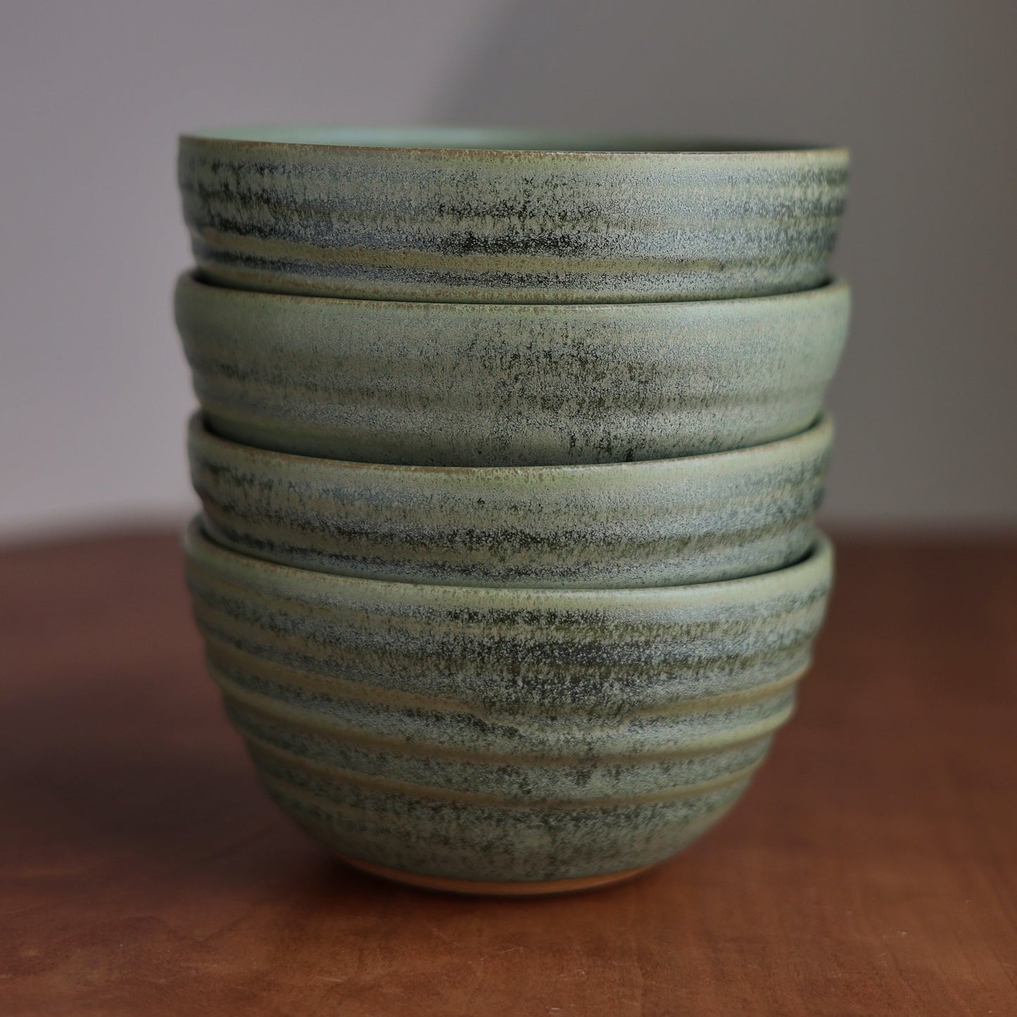 Stack of green ceramic bowls on a wooden surface with a plain background