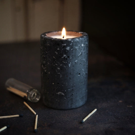 Black terrazzo vessel with pure soy candle and matches on a dark surface