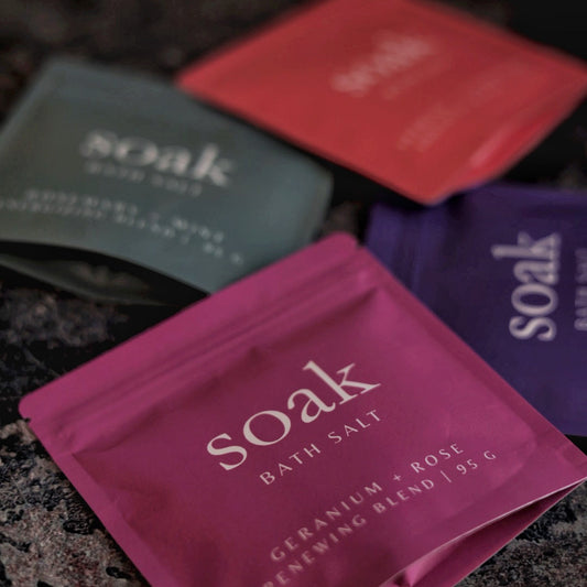 Three 'soak' bath salt packages in different colors on a textured surface.