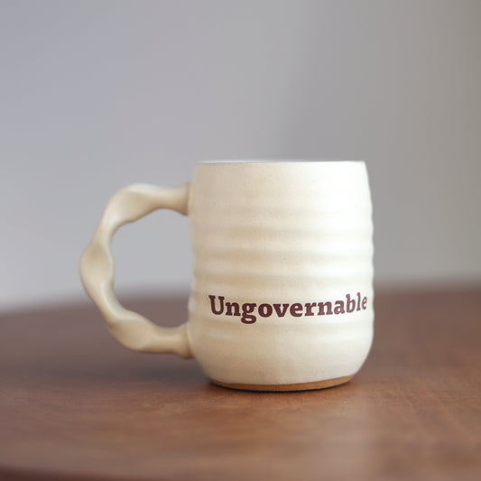 White mug with 'Ungovernable' text on a wooden surface