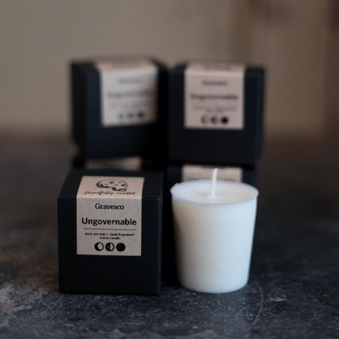 White candle in a black box with 'Graveco' branding on a dark surface.
