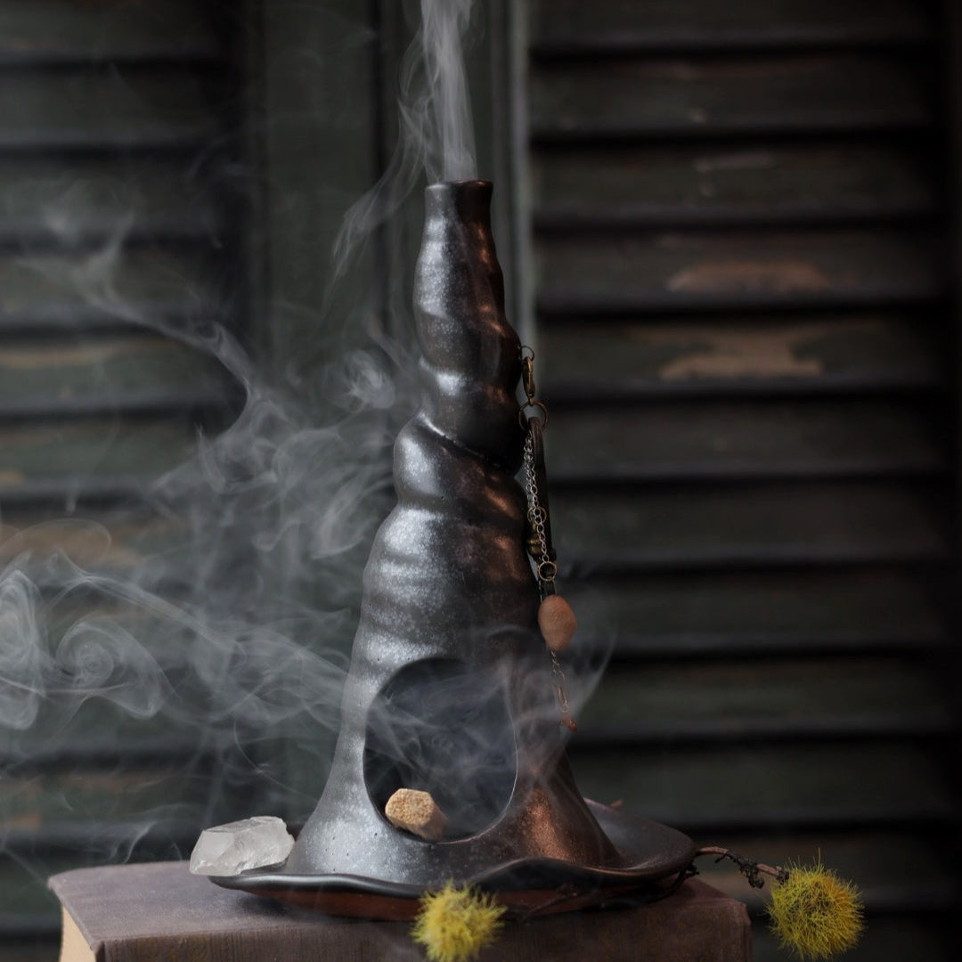 Smoldering witch hat incense burner on top of books with a dark background