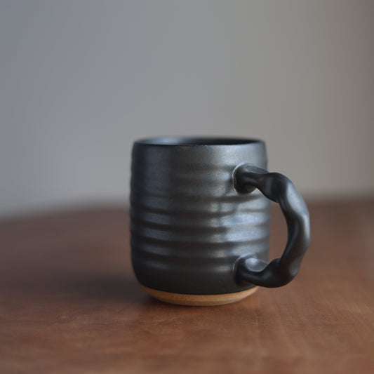 A black handmade companion mug on a wooden table with a blurred background
