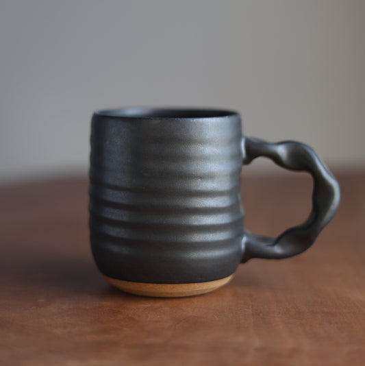 A black handmade mug on a wooden table with a blurred background