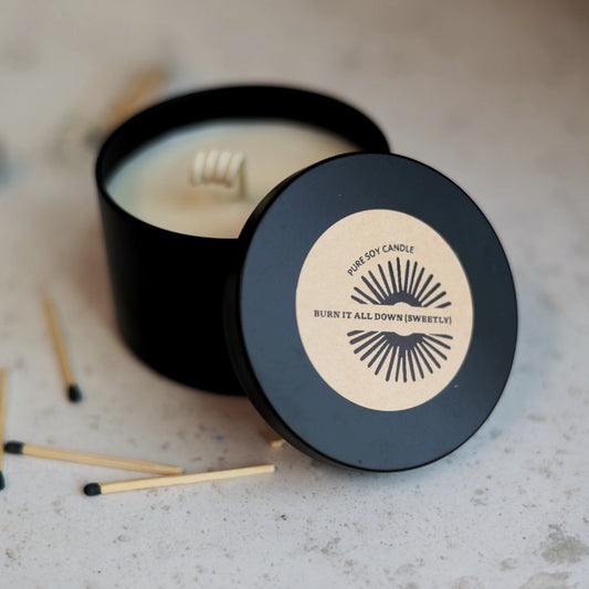 Black soy candle with a beige label on a gray surface with matches.