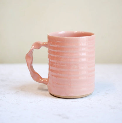 Pink ceramic mug on a white surface with a neutral background