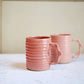 Two pink ceramic mugs on a white surface with a neutral background