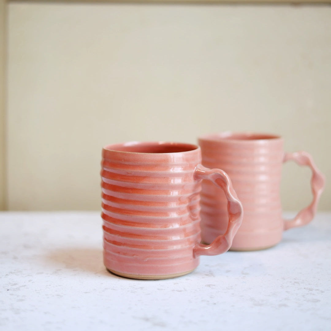 Two pink ceramic mugs on a white surface with a neutral background