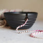 Black ceramic bowl with a pink and white string on a light surface.