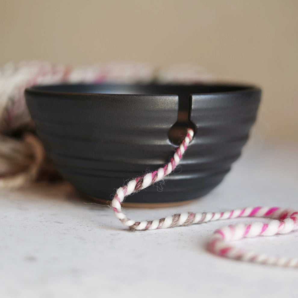 Black ceramic bowl with a pink and white string on a light surface.