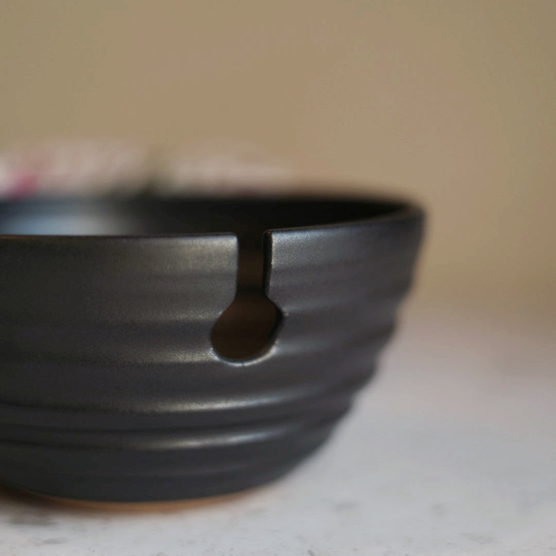 Black ceramic yarn bowl on a light surface with a blurred background