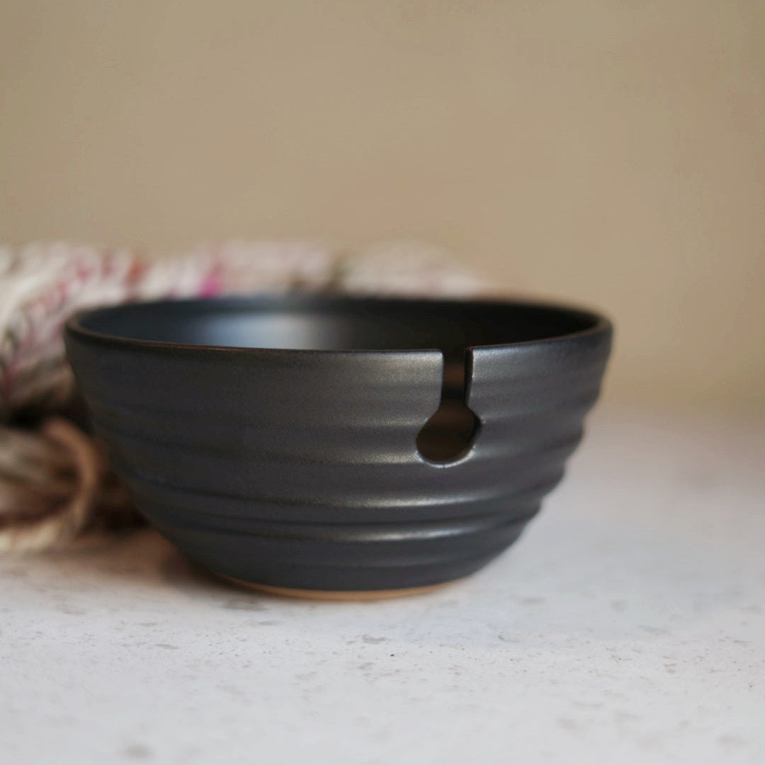 Black ceramic yarn bowl on a light surface with a neutral background