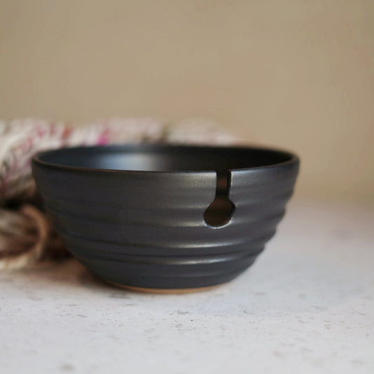 Black ceramic yarn bowl on a light surface with a neutral background