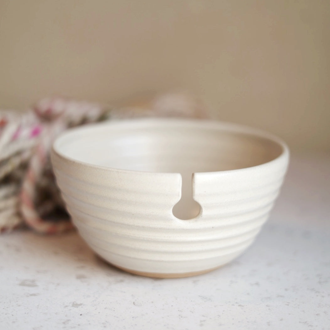 cream ceramic yarn bowl on a textured surface with a blurred background