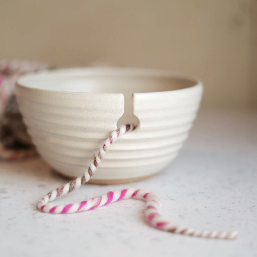 Cream ceramic yarn bowl with a pink and white striped straw on a light surface.