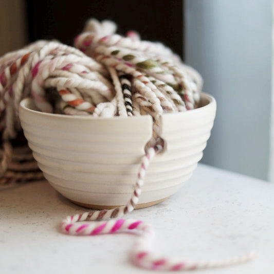 Ball of yarn in a ceramic yarn bowl on a light surface