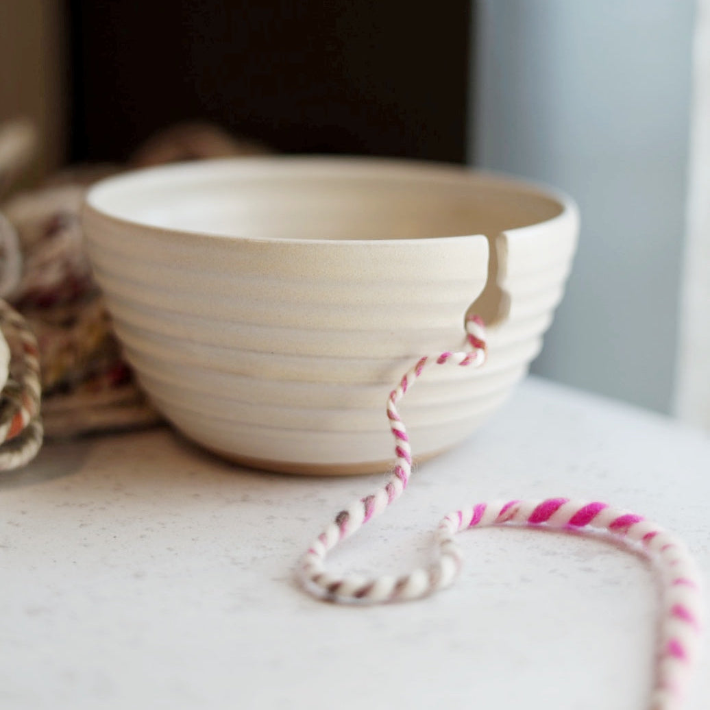 White ceramic yarn bowl with a pink and white string on a light surface