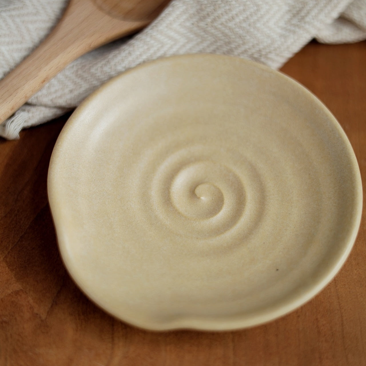 Beige ceramic dish with spiral design on a wooden surface