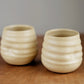 Two beige ceramic cups with textured surface on a wooden surface.