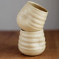 Two beige ceramic cups stacked on a wooden surface with a neutral background