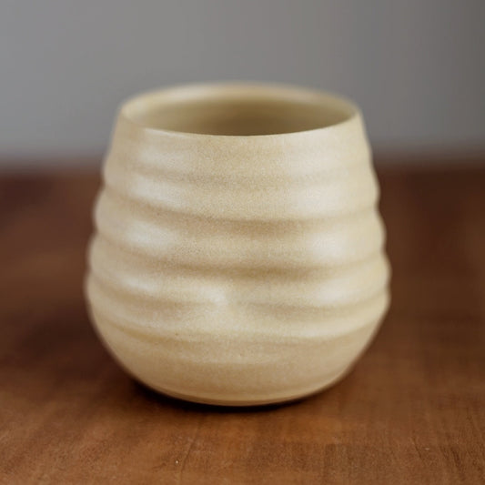 Beige ceramic cup with textured surface on a wooden surface