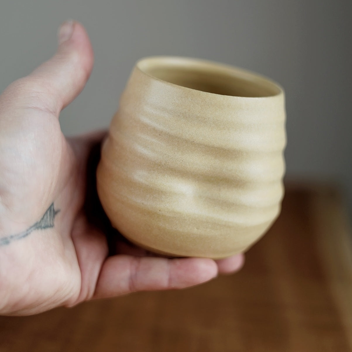 Hand holding a small ceramic cup against a neutral background