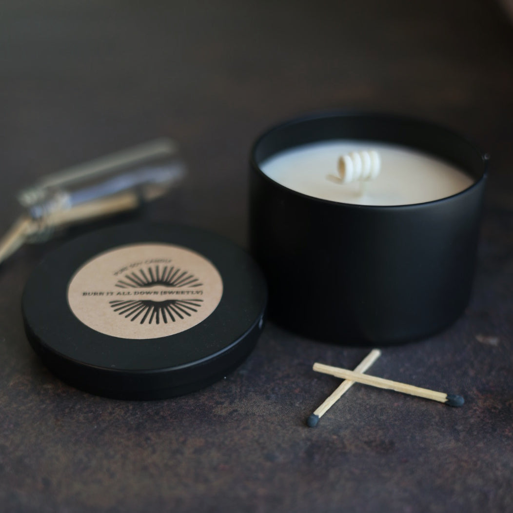 Black candle in a container with matches on a dark surface