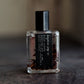 Small Palo Santo perfume bottle with a black cap on a dark surface