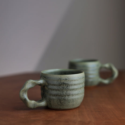 Two green ceramic mugs on a wooden surface with a neutral background