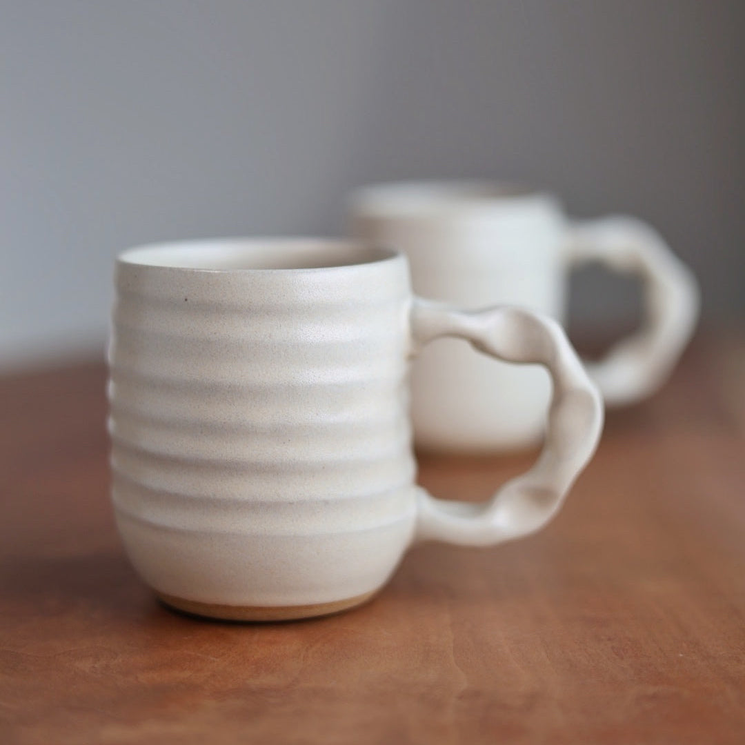 Two ceramic mugs on a wooden surface with a blurred background