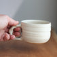Hand holding a white ceramic cup against a neutral background