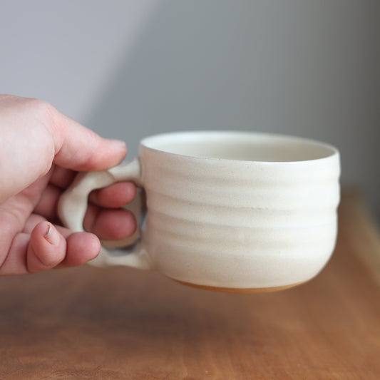 Hand holding a white ceramic cup against a neutral background