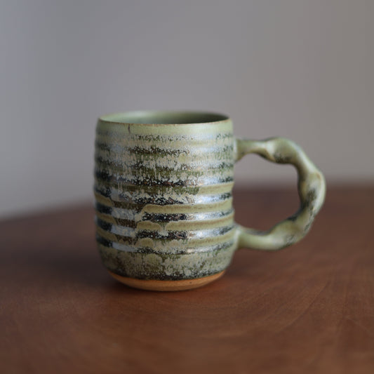 Moss green ceramic mug with textured surface on a blurred background