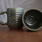 Two ceramic mugs with textured surfaces on a wooden surface.
