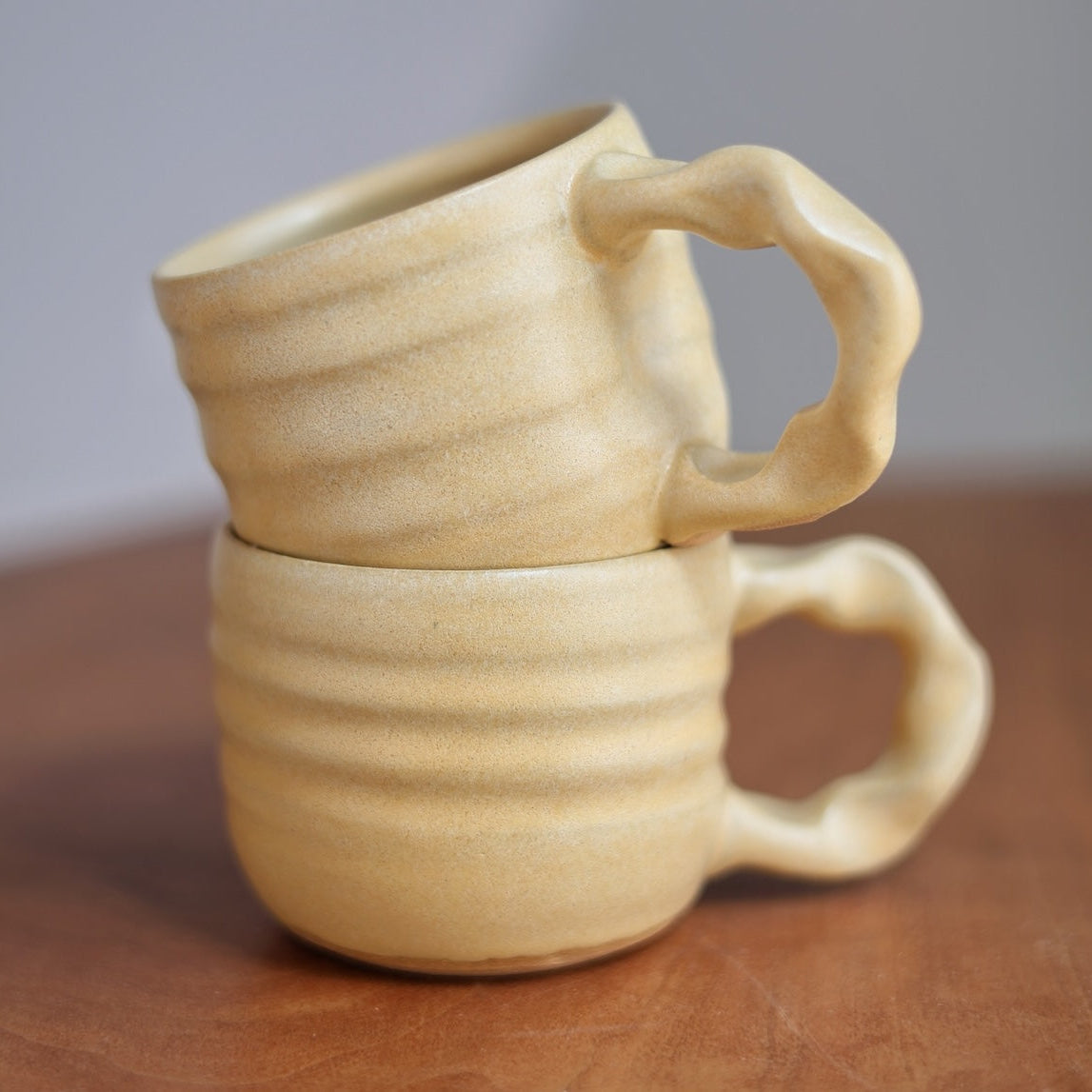 Two beige ceramic mugs stacked on a wooden surface with a neutral background