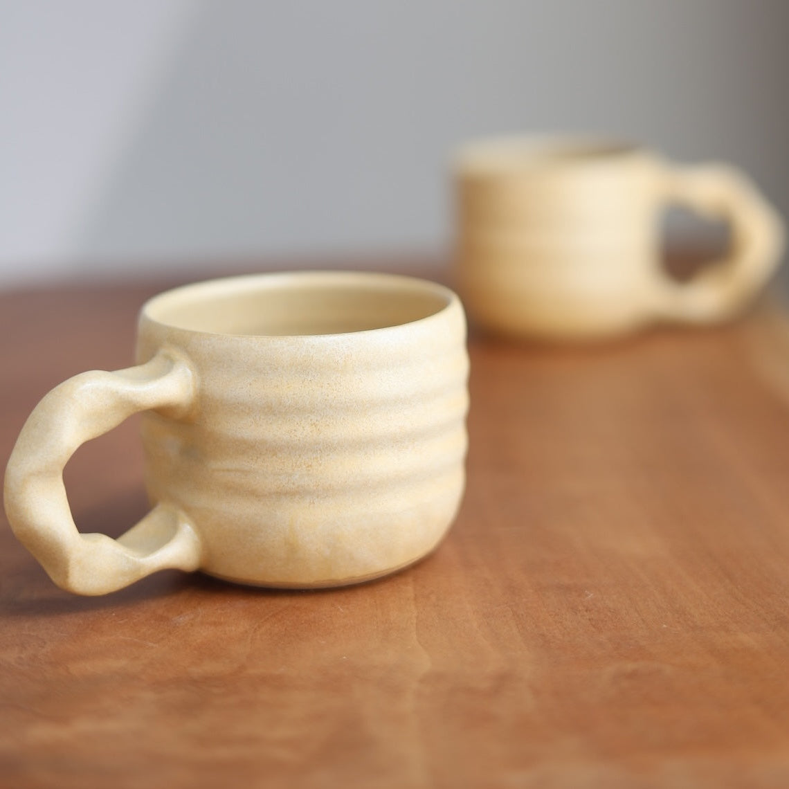 Two ceramic mugs on a wooden surface with a blurred background