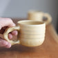 Hand holding a ceramic mug on a wooden surface with another mug in the background.