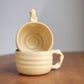 Beige ceramic cup stacked on a matching ceramic cup on a wooden surface