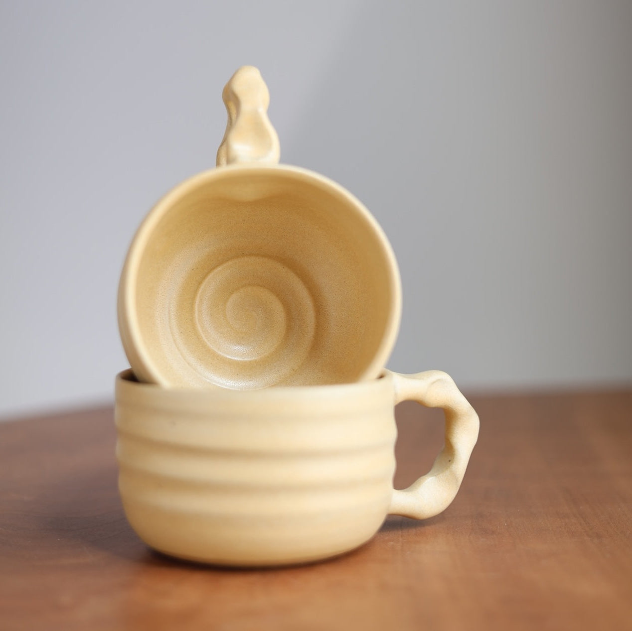 Beige ceramic cup stacked on a matching ceramic cup on a wooden surface