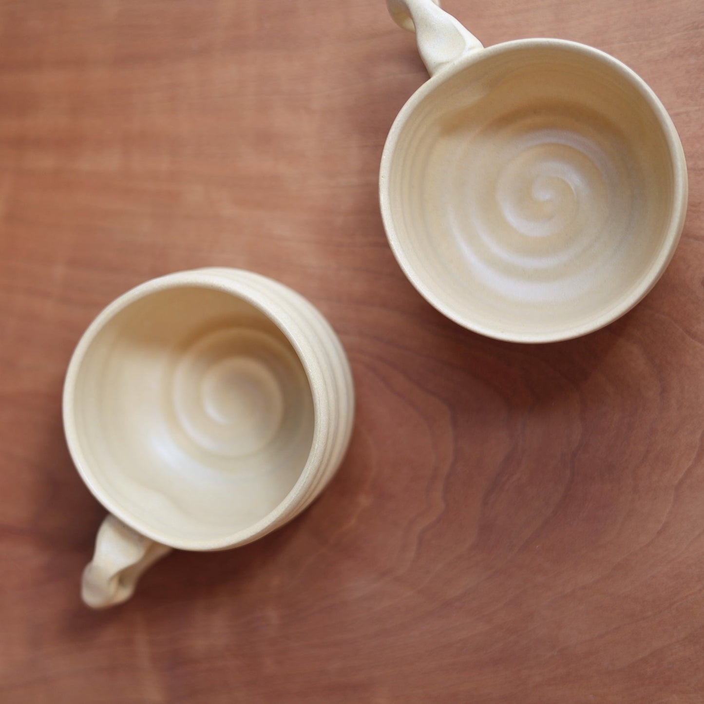 Two ceramic mugs with spiral designs on a wooden surface