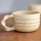 Beige ceramic mug on a wooden surface with a blurred background