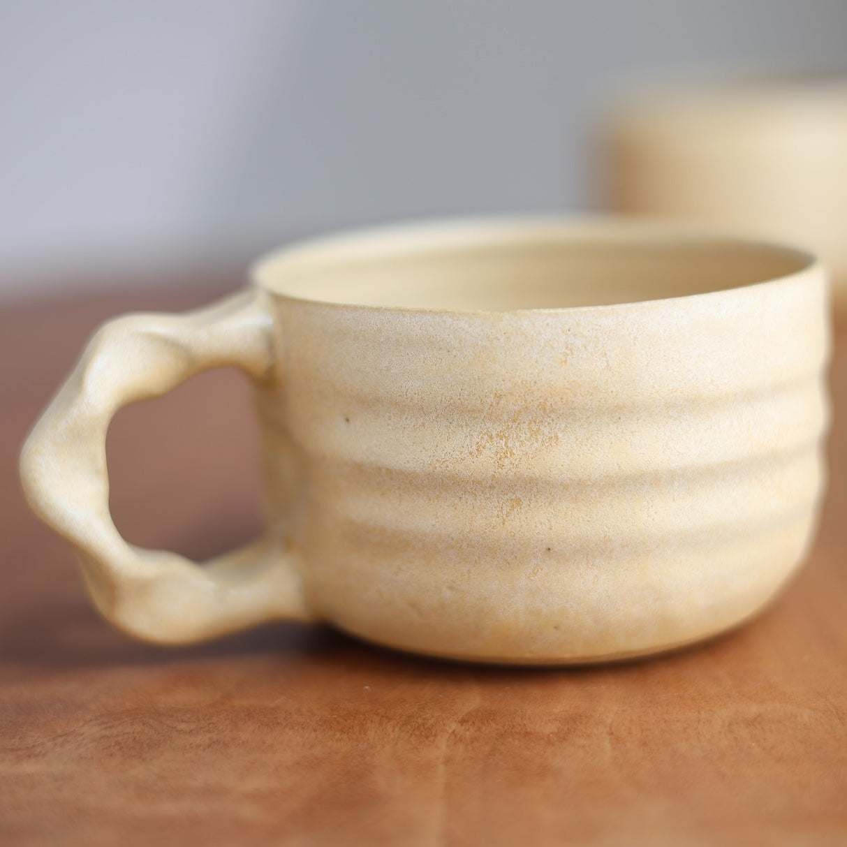 Beige ceramic mug on a wooden surface with a blurred background