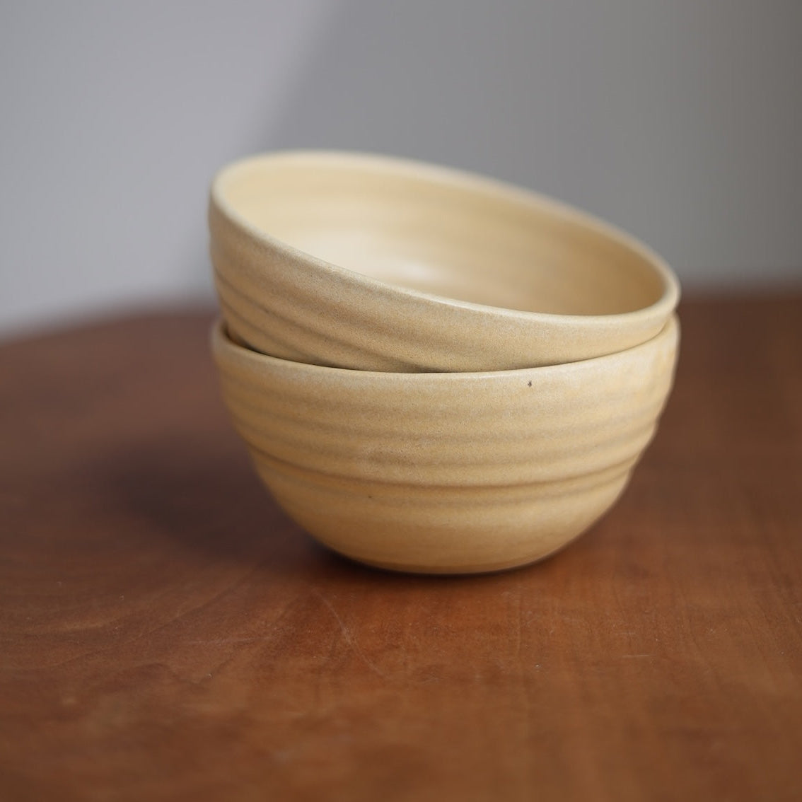 Two beige ceramic bowls stacked on a wooden surface with a neutral background