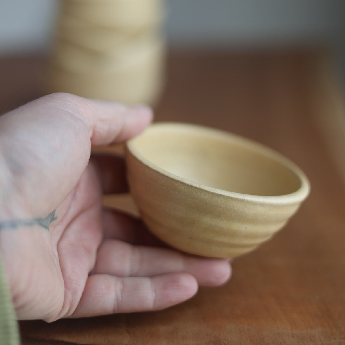 Hand holding a small ceramic bowl on a wooden surface